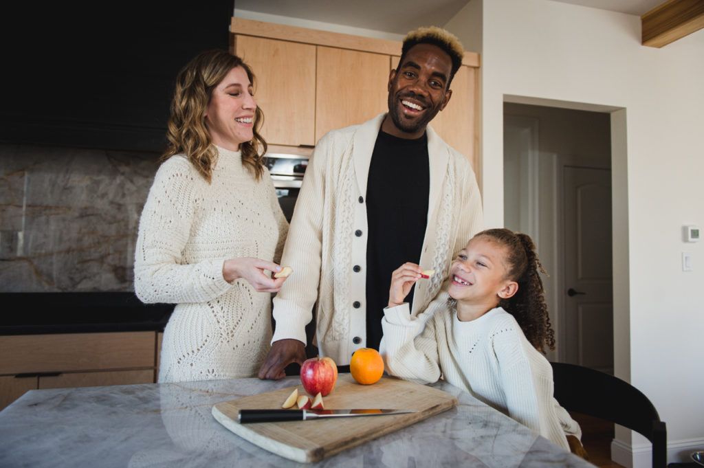 Family smiling together in a kitchen, preparing food. Apple and orange on the counter.
