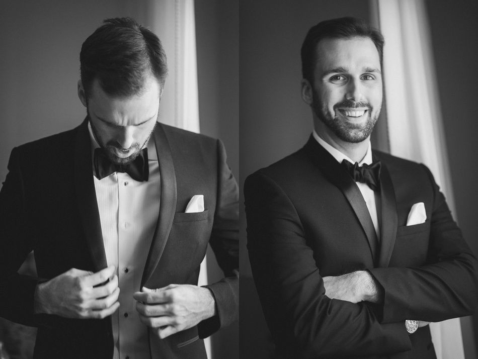 Bride and groom on rocky shoreline, ocean and blue sky background. Groom in suit, bride in white dress, looking at each other.