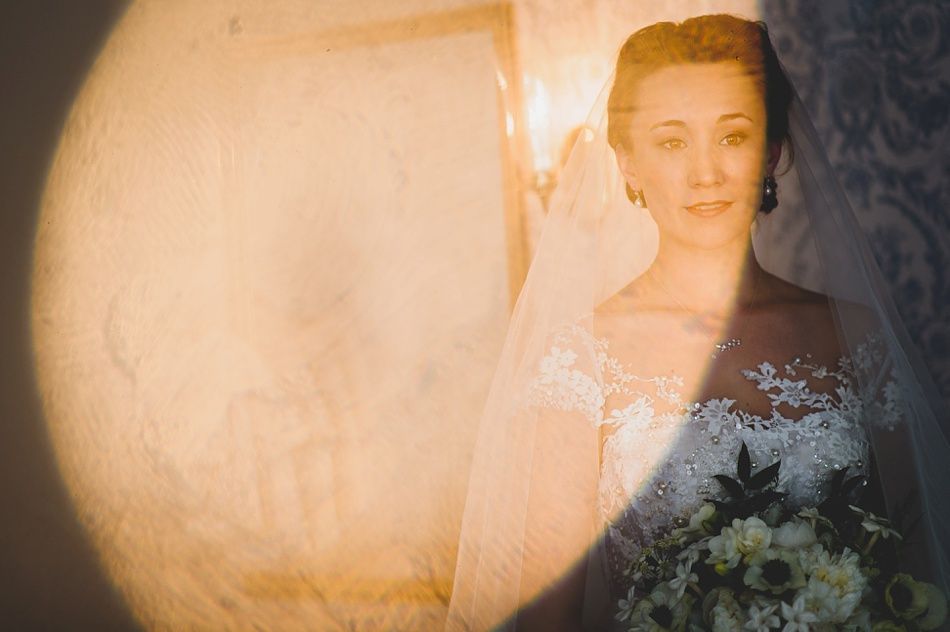 Bride with arms up, making a funny face, groom looking at his hand, cake cutting in background.