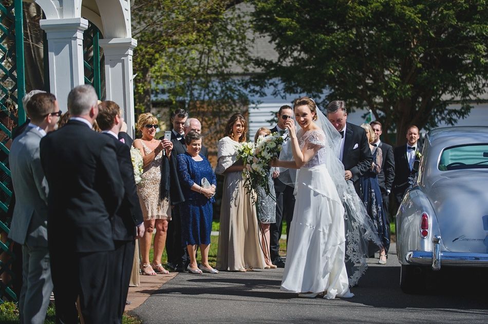 Bride with arms up, making a funny face, groom looking at his hand, cake cutting in background.