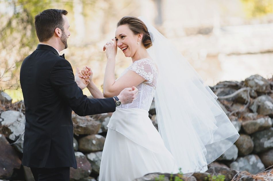Bride with arms up, making a funny face, groom looking at his hand, cake cutting in background.