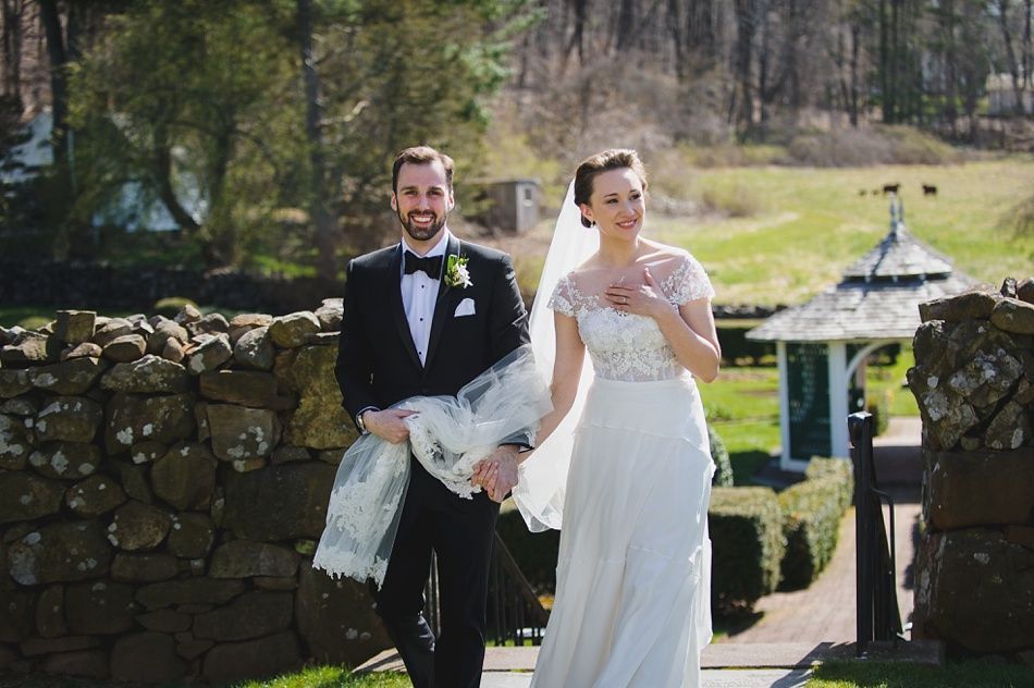 Bride with arms up, making a funny face, groom looking at his hand, cake cutting in background.