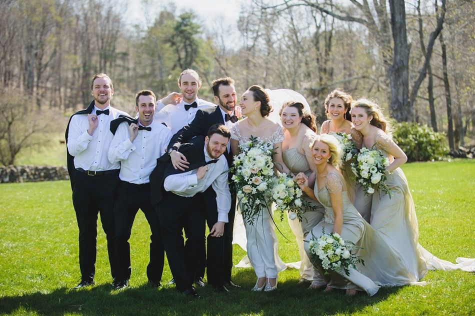 Bride with arms up, making a funny face, groom looking at his hand, cake cutting in background.