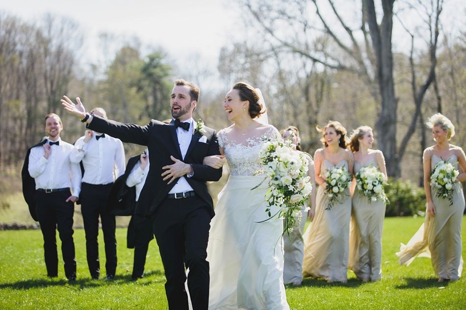 Bride with arms up, making a funny face, groom looking at his hand, cake cutting in background.