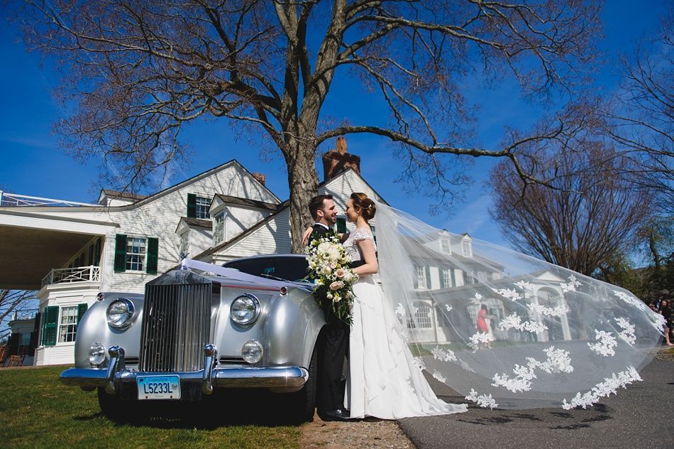 Bride with arms up, making a funny face, groom looking at his hand, cake cutting in background.