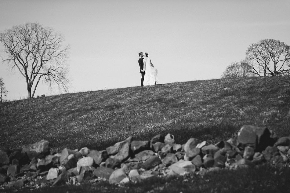 Bride with arms up, making a funny face, groom looking at his hand, cake cutting in background.