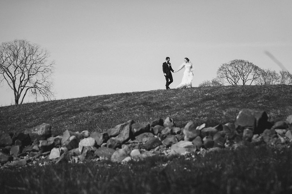 Bride with arms up, making a funny face, groom looking at his hand, cake cutting in background.