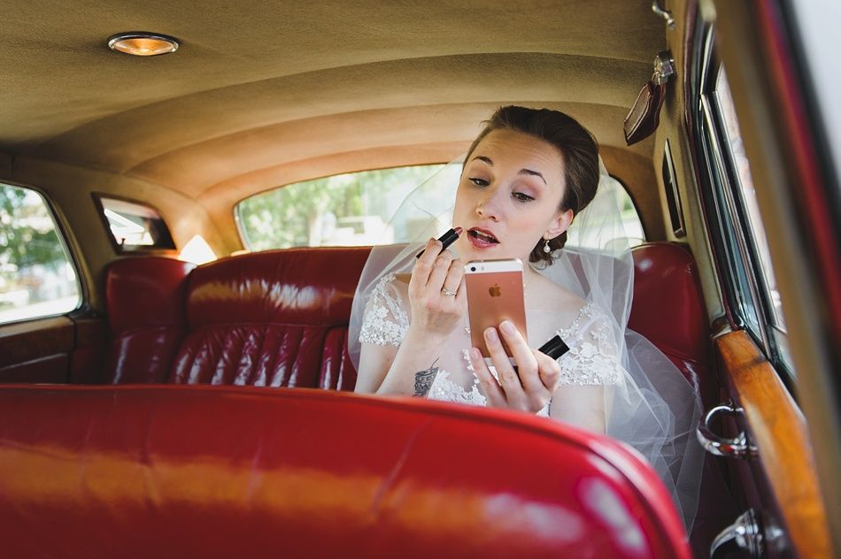 Bride with arms up, making a funny face, groom looking at his hand, cake cutting in background.