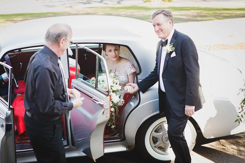 Bride with arms up, making a funny face, groom looking at his hand, cake cutting in background.