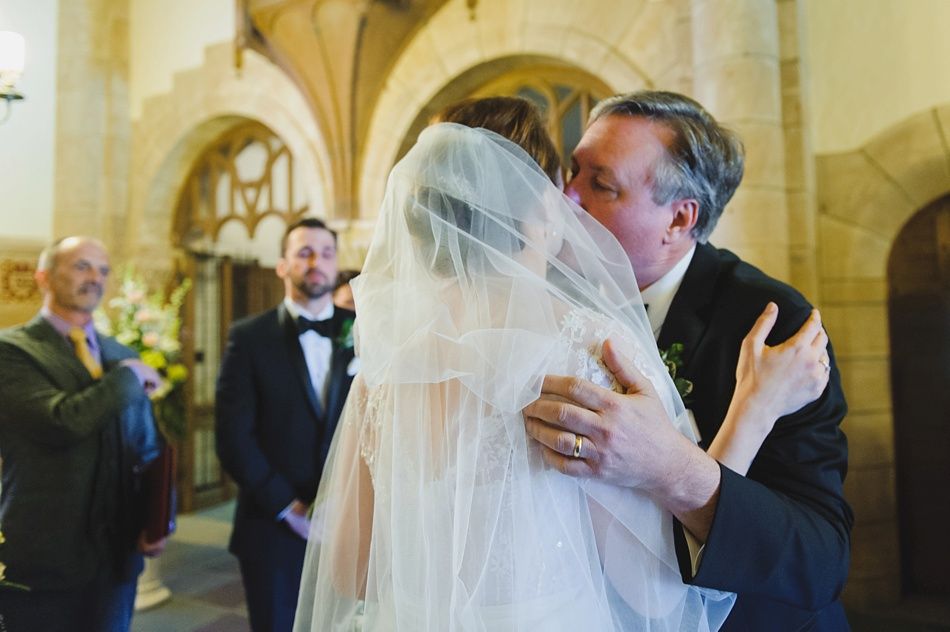 Bride with arms up, making a funny face, groom looking at his hand, cake cutting in background.