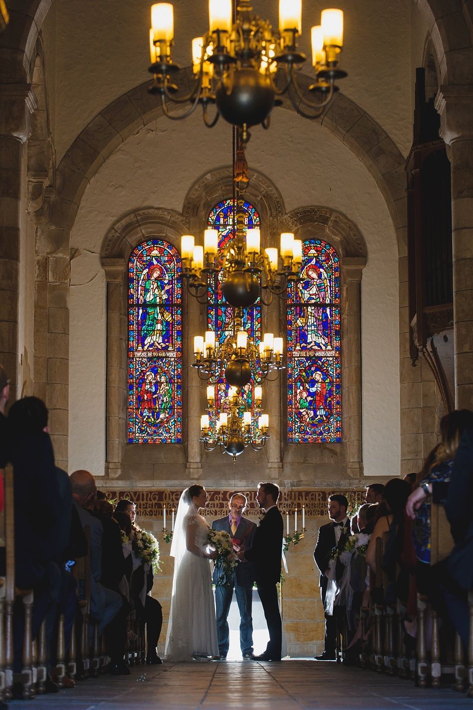 Bride with arms up, making a funny face, groom looking at his hand, cake cutting in background.