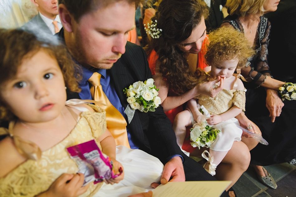 Bride with arms up, making a funny face, groom looking at his hand, cake cutting in background.