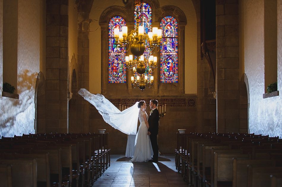 Bride with arms up, making a funny face, groom looking at his hand, cake cutting in background.
