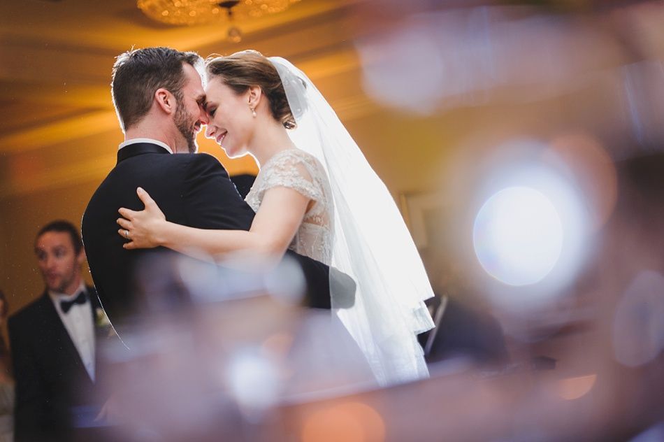 Bride with arms up, making a funny face, groom looking at his hand, cake cutting in background.