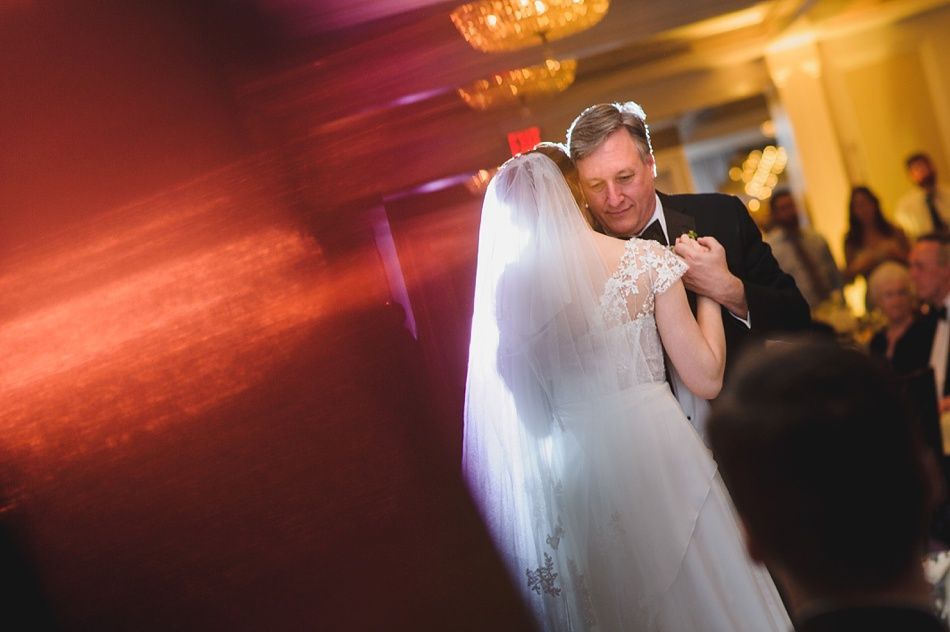 Bride with arms up, making a funny face, groom looking at his hand, cake cutting in background.