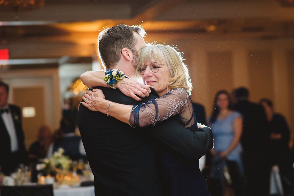 Bride with arms up, making a funny face, groom looking at his hand, cake cutting in background.