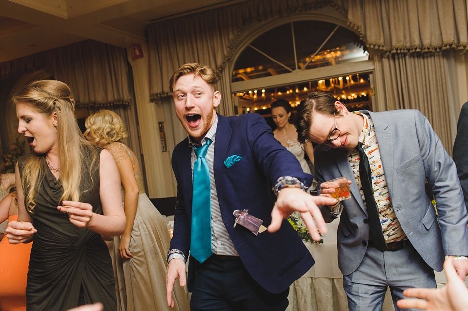 Bride with arms up, making a funny face, groom looking at his hand, cake cutting in background.