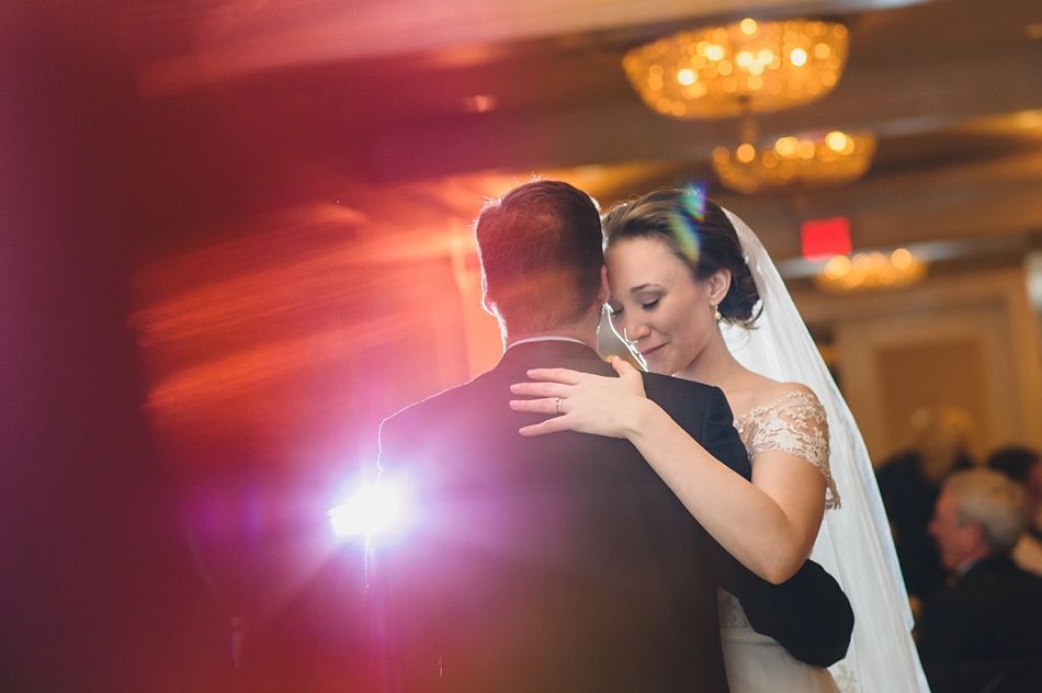 Bride with arms up, making a funny face, groom looking at his hand, cake cutting in background.