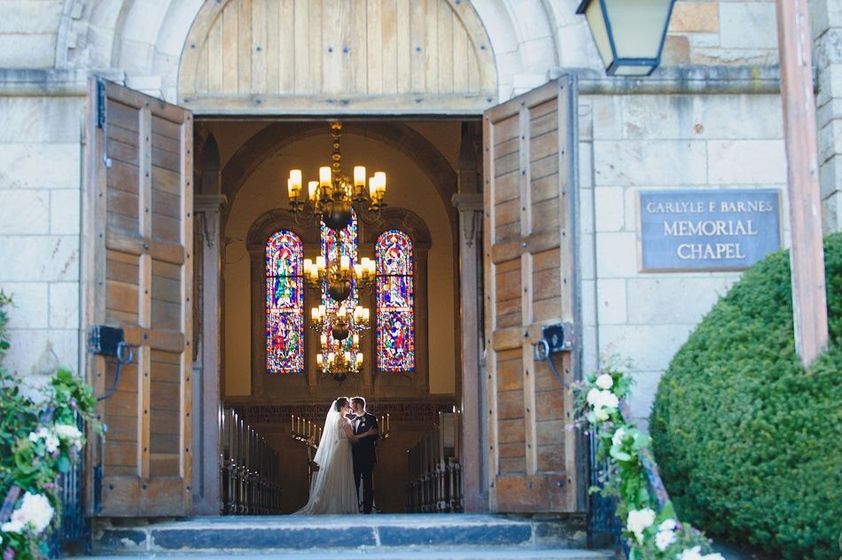 Bride with arms up, making a funny face, groom looking at his hand, cake cutting in background.