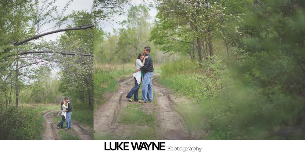 Couple embracing on a muddy road surrounded by trees and greenery.