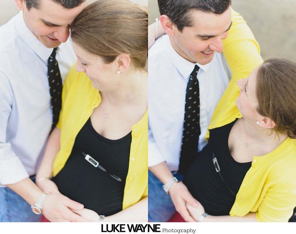 Couple expecting a baby, smiling, looking at pregnant belly. The woman wears yellow cardigan over black top.