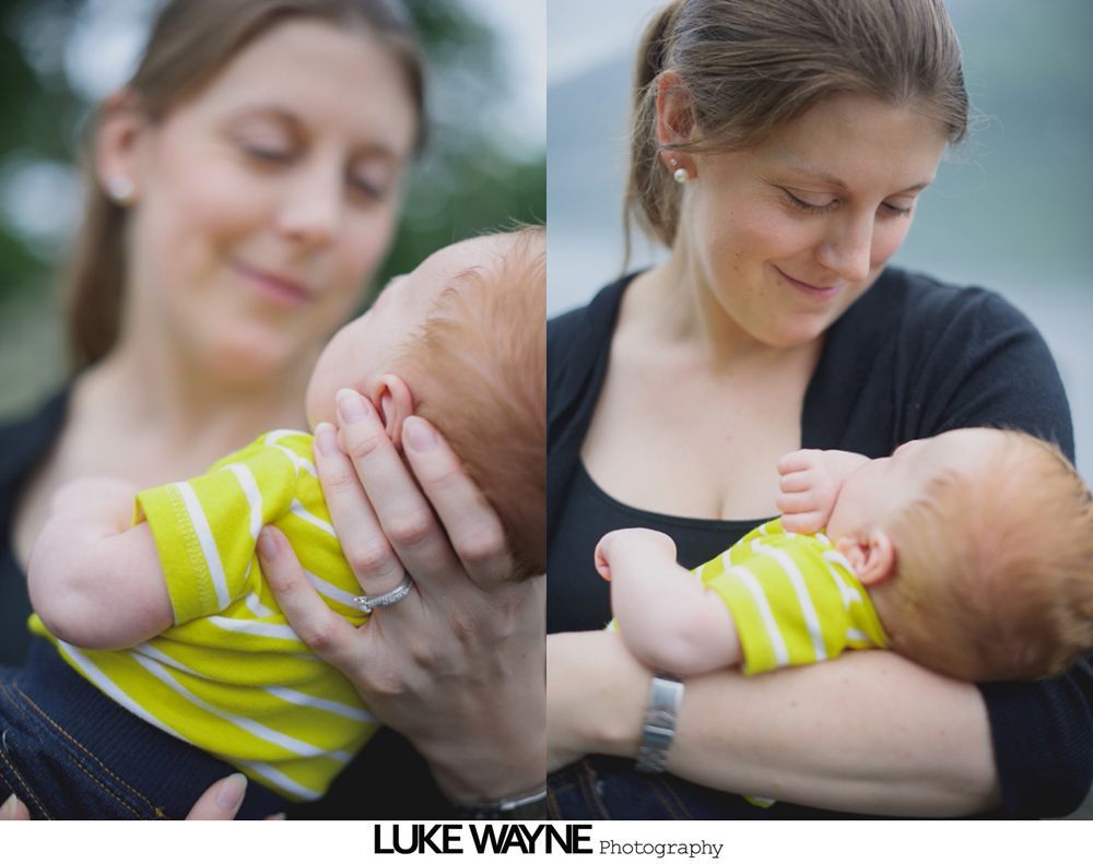 Woman holding and gazing at a baby in a yellow striped shirt. Outdoor setting, soft focus.