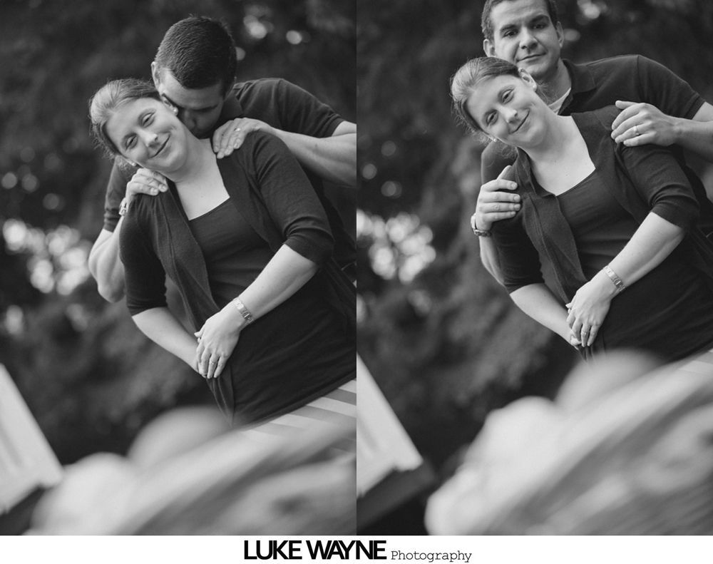 Couple embracing outdoors; man kissing woman's neck, smiling. Black and white.