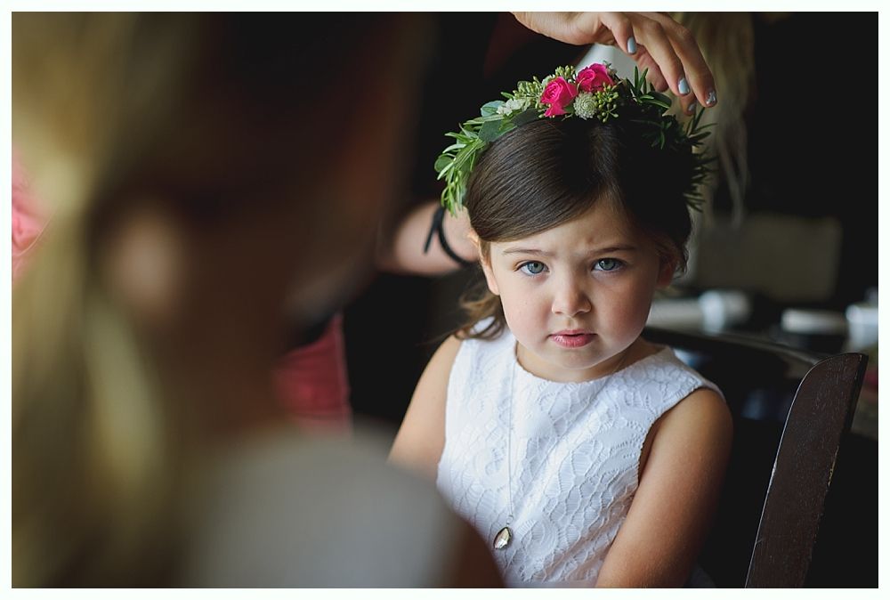 Wedding party on a beach with blue sky. Bride and groom embrace, others stand nearby. Dark blue dresses and jackets.
