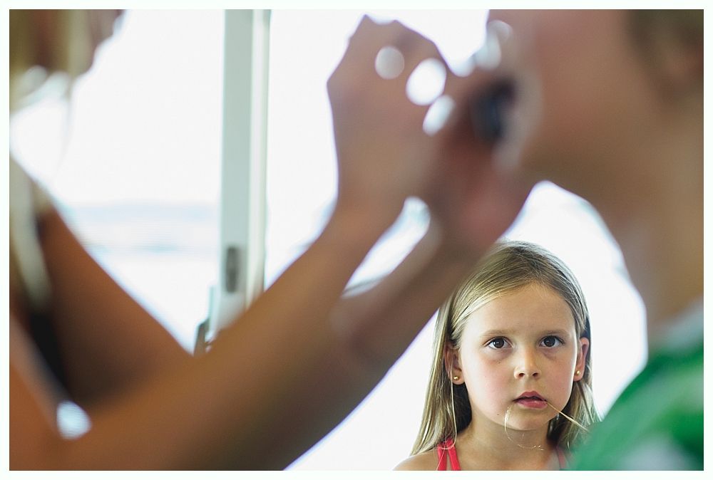 Bride and groom embrace on rocks by the ocean at sunset. The groom wears a blue suit, the bride a white dress.