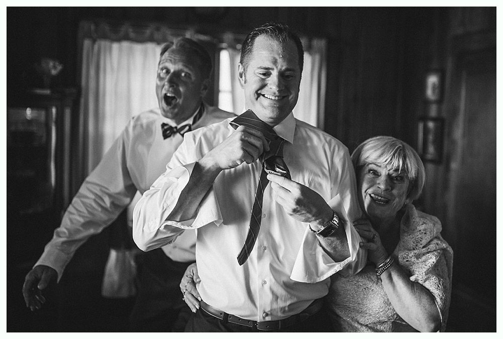 Bride with arms up, making a funny face, groom looking at his hand, cake cutting in background.