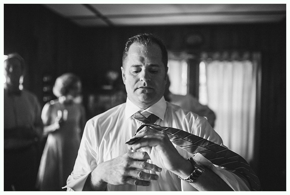 Bride with arms up, making a funny face, groom looking at his hand, cake cutting in background.