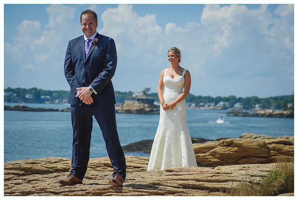 Bride with arms up, making a funny face, groom looking at his hand, cake cutting in background.