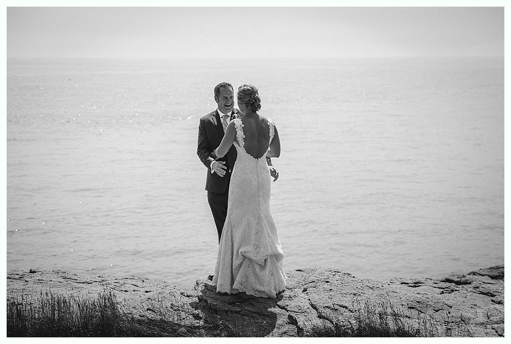 Bride with arms up, making a funny face, groom looking at his hand, cake cutting in background.