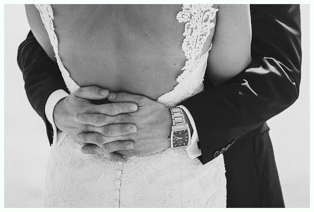 Bride with arms up, making a funny face, groom looking at his hand, cake cutting in background.
