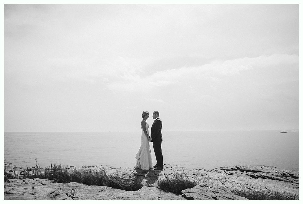 Bride with arms up, making a funny face, groom looking at his hand, cake cutting in background.