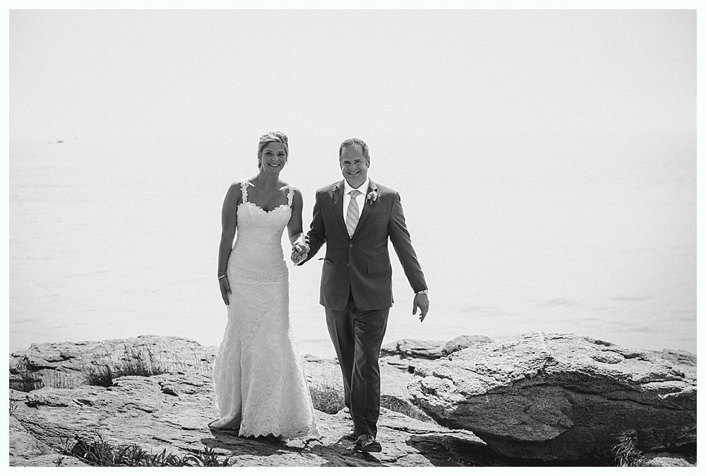 Bride with arms up, making a funny face, groom looking at his hand, cake cutting in background.