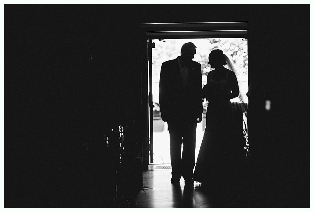 Bride with arms up, making a funny face, groom looking at his hand, cake cutting in background.