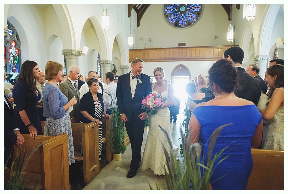 Bride with arms up, making a funny face, groom looking at his hand, cake cutting in background.