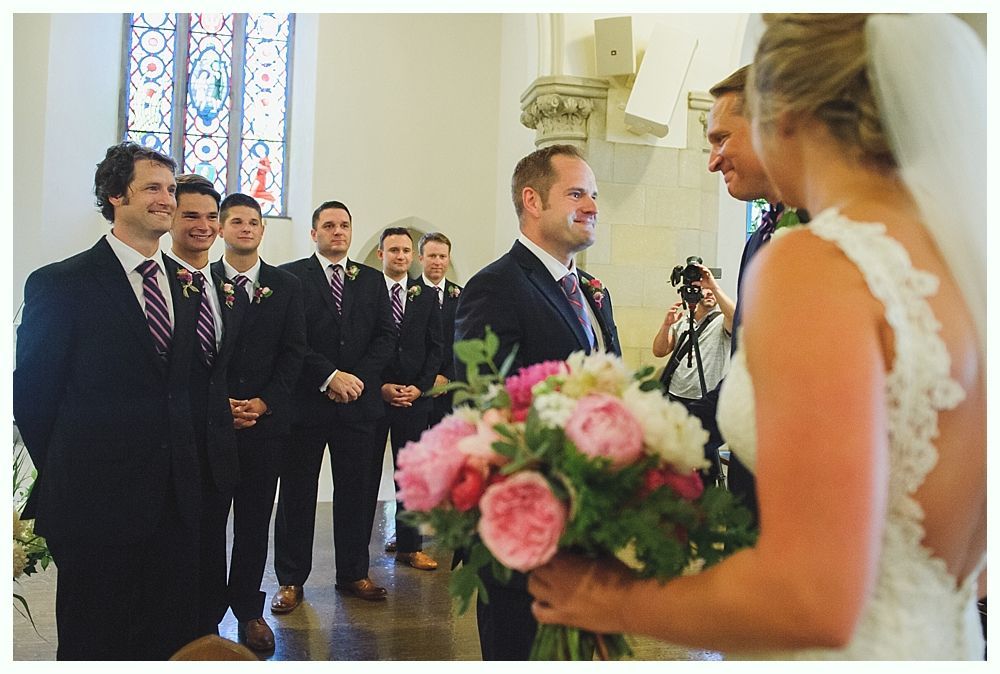 Bride with arms up, making a funny face, groom looking at his hand, cake cutting in background.