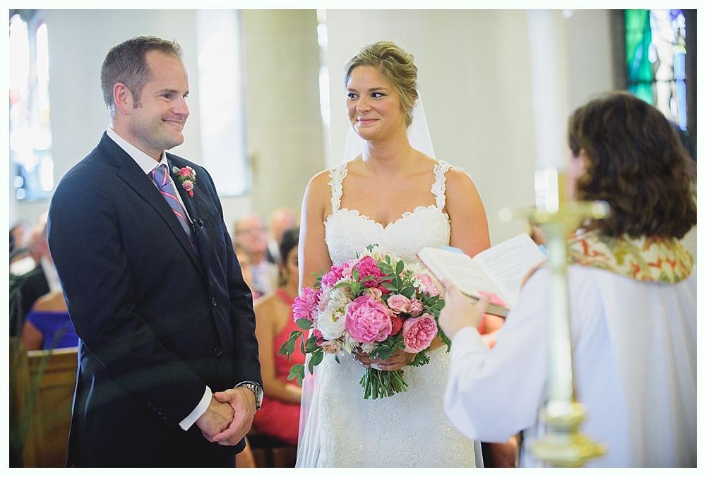 Bride with arms up, making a funny face, groom looking at his hand, cake cutting in background.