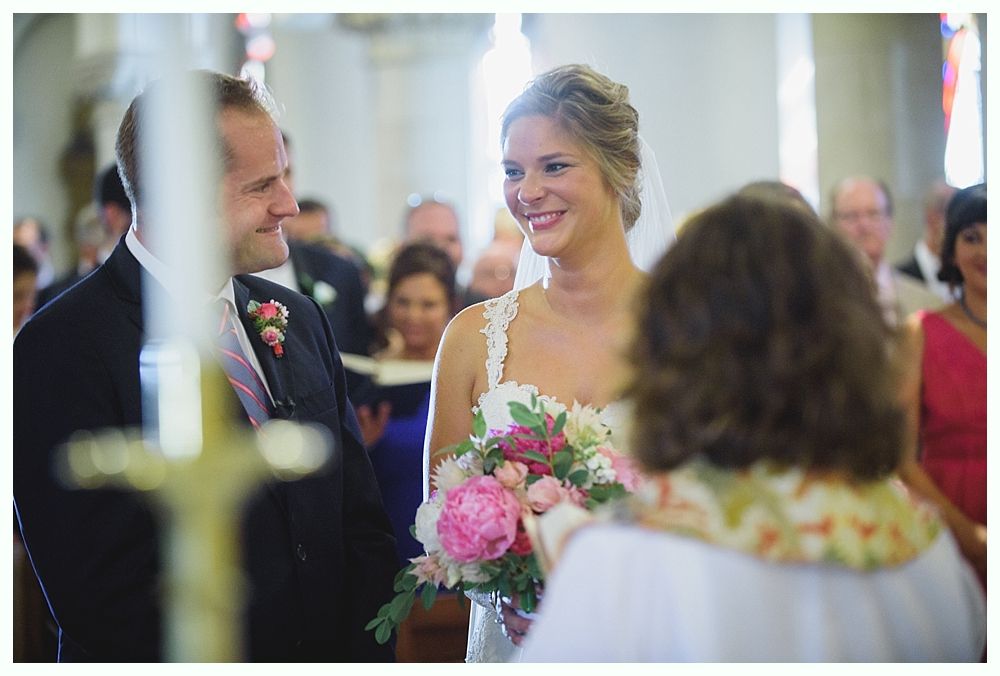 Bride with arms up, making a funny face, groom looking at his hand, cake cutting in background.