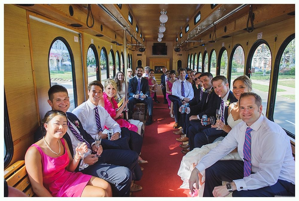 Bride with arms up, making a funny face, groom looking at his hand, cake cutting in background.