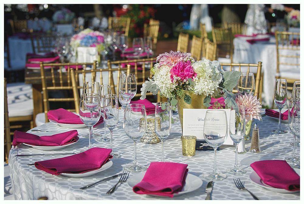 Bride with arms up, making a funny face, groom looking at his hand, cake cutting in background.