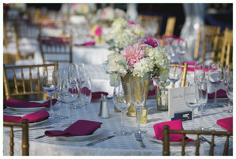 Bride with arms up, making a funny face, groom looking at his hand, cake cutting in background.