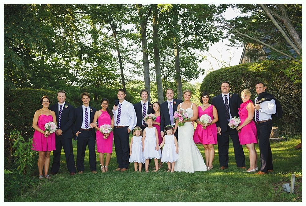 Bride with arms up, making a funny face, groom looking at his hand, cake cutting in background.