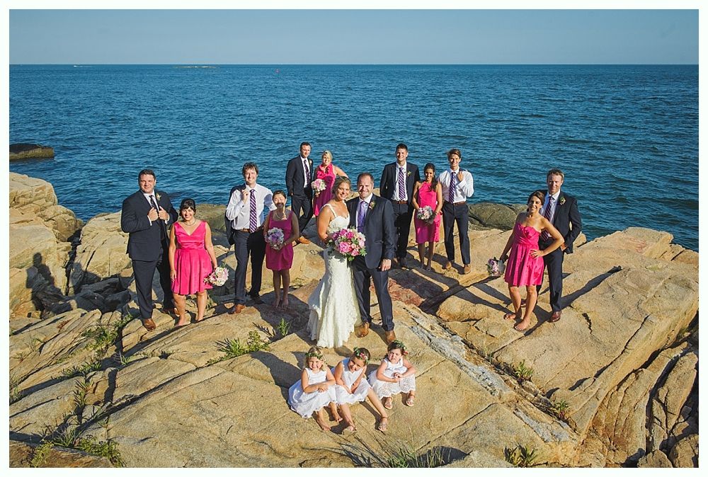 Bride with arms up, making a funny face, groom looking at his hand, cake cutting in background.