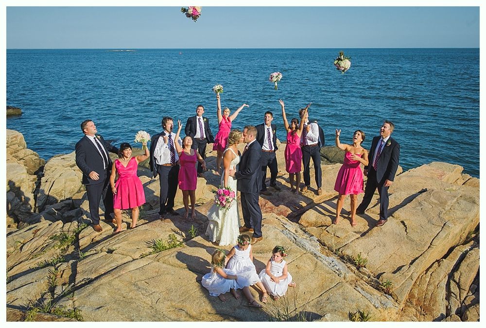 Bride with arms up, making a funny face, groom looking at his hand, cake cutting in background.