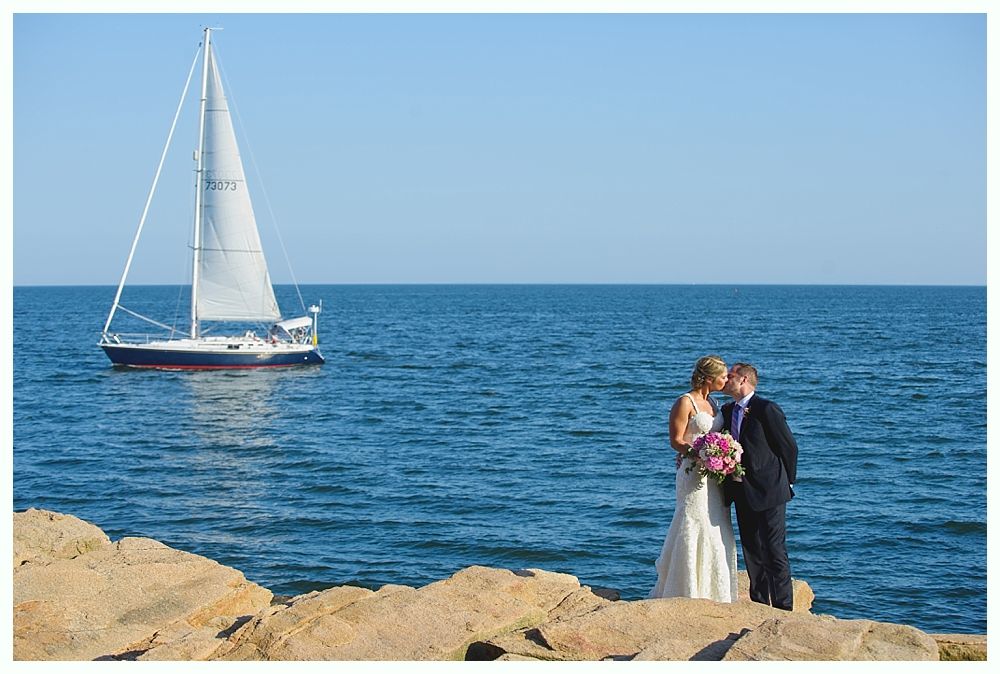 Bride with arms up, making a funny face, groom looking at his hand, cake cutting in background.