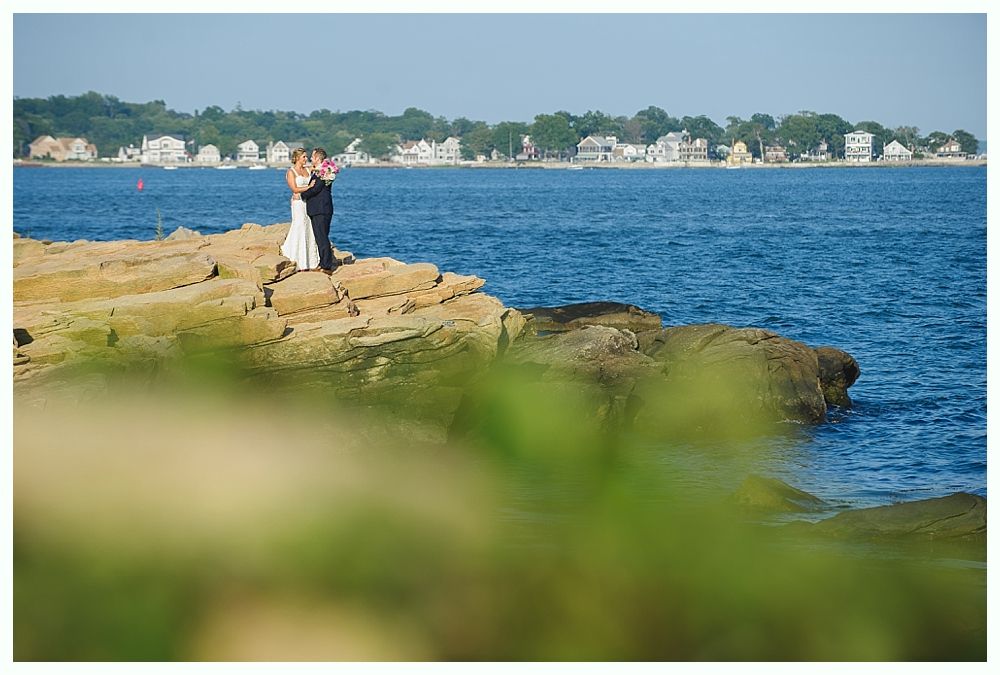 Bride with arms up, making a funny face, groom looking at his hand, cake cutting in background.