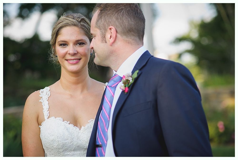 Bride with arms up, making a funny face, groom looking at his hand, cake cutting in background.